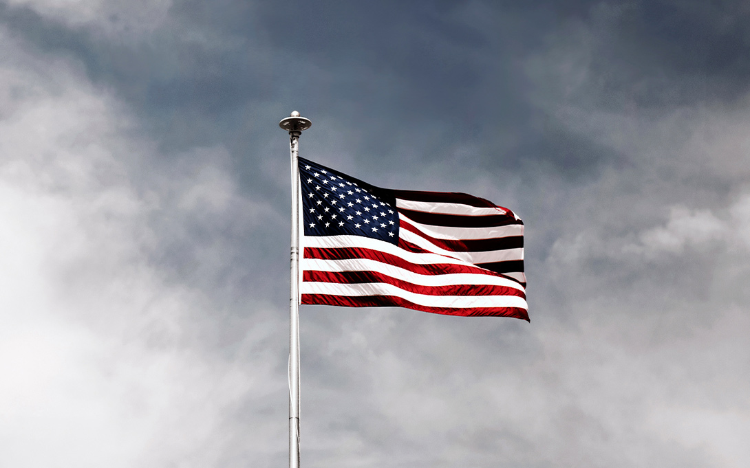 American flag waving, gray sky